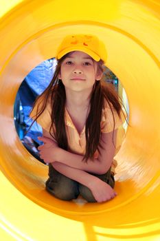 Beautiful little girl playing inside a yellow tube at playground