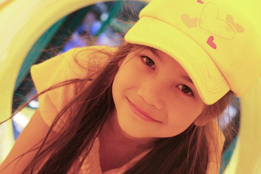 Beautiful little girl playing inside a yellow tube at playground