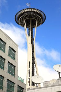 The Seattle space needle tower with a building and satellite dishes in the foreground.