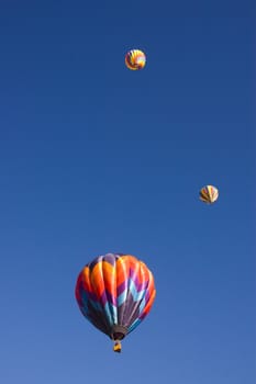 three of the balloons at the Taos balloon festival sailing upwards into a deep blue sky