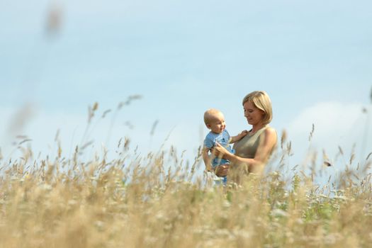 Young woman with baby on her shoulders in a country field of tall grass.