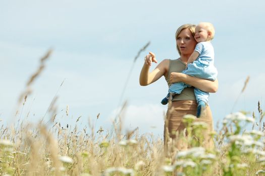 Young woman with baby on her shoulders in a country field of tall grass.