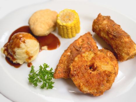 Fried chicken breast, banana and pineaplle, with mashed potatoes, corn and bread on a white plate