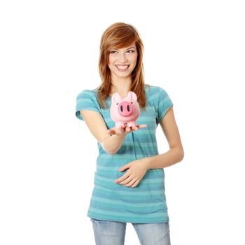 Young teen woman showing her pink piggy bank , looking left . Isolated