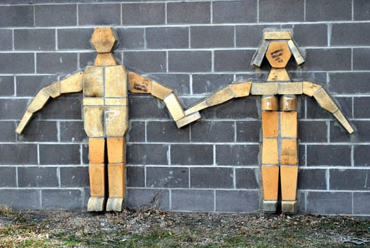 Wooden couple standing against a gray brick wall.