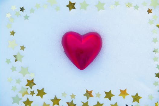 a red  heart and golden snow stars on a real snowy icy surface