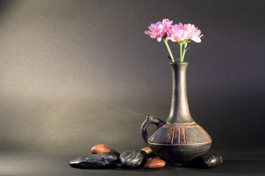 Ancient ceramic vase with nice pink flower near stones on dark background