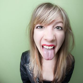 Cute young woman sticks out her tongue over green background