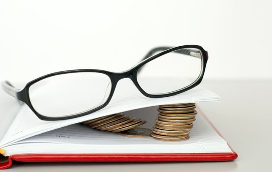 Glasses, book and piles of coins