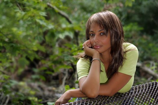 A beautiful mature black woman soaks up some atmosphere on a park bench amidst lush tropical vegetation outdoors, looking directly into the camera.