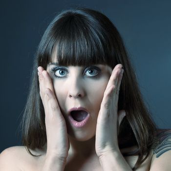 Portrait of a lovely woman with a astonish expression against a grey background 