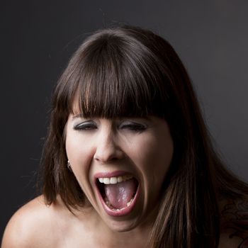 Close-up portrait of a desperate woman shouting with something, against a grey background