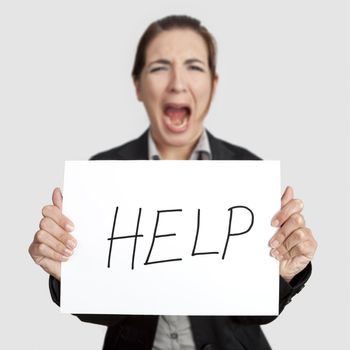 Stressed business woman imploring for help, holding a cardboard with the message "Help". Focus is on the cardboard