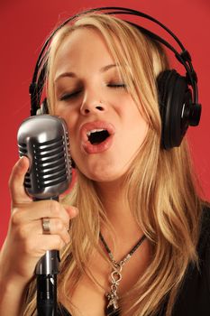 Photo of a beautiful young blond wearing headphones and singing into a vintage microphone.