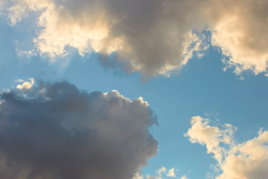 Cloudscape, dark gray and light yellowish clouds on the blue sky