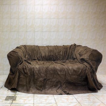 Old and dirty couch with wrinkles stands in bathroom on glazed tiles near the drain aperture. High dymamic range (HDR)