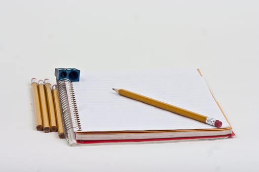 Note book with pencils and a sharpner on a white background.