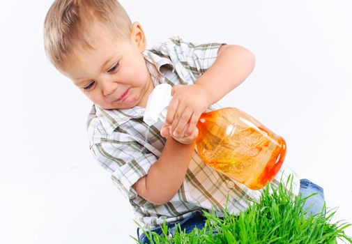 Cute boy watering the green grass. In the studio