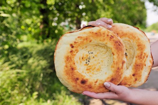 Two traditional flat cakes from tandoor in hands.