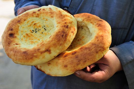 Two traditional flat cakes from tandoor in hands.