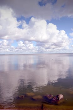 Reflections of the sky on a calm lake water. Stones underwater.