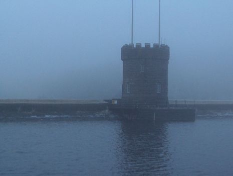 A fortification along the waters of a lake in the Brecon Beacons in Wales on a blue foggy day.