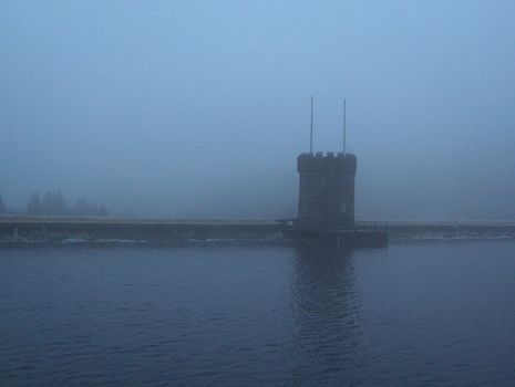 A fortification along the waters of a lake in the Brecon Beacons in Wales on a blue foggy day.