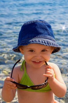 A very cute little girl with beautiful smile trying to wear her mom's sun glasses at the beach