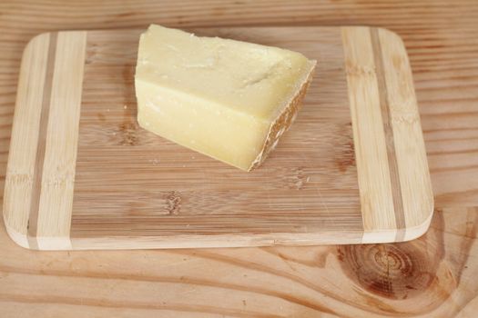 Parmesan cheese with grater on wooden chopping board.