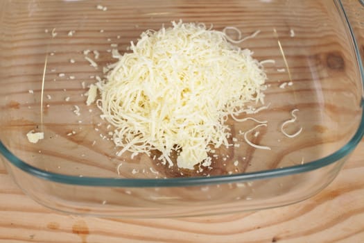 Parmesan cheese with grater on wooden chopping board.