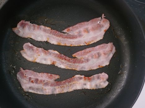 strips of bacon frying in a skillet