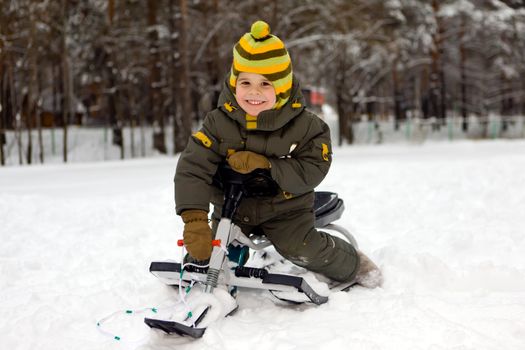 The smiling boy sits on a sledge
