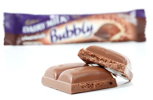 Cadbury Dairy Milk Bubbly 40g (892kj) Dairy milk chocolate with a light bubbly light aerated centre. Showing packaging in background and pieces of the chocolate in focus in the foreground.  Photographed in studio on a white background. 