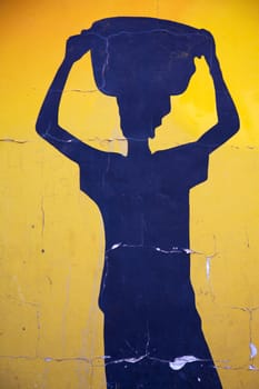 Blue shape of an African woman carrying something on her head on yellow background in Bamako