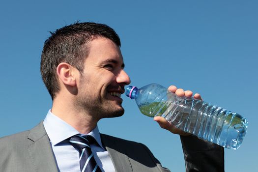 handsome businessman drinking water with bottle in blue sky