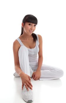 Beautiful smiling young woman wearing white exercise tracksuit pants, sports shoes and tanktop sits on the floor casually.  White background.