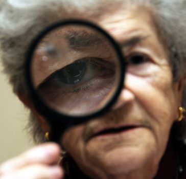 Old senior woman looking through magnifying glass