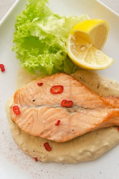 Grilled salmon steak with greens, lemon, sauce and pepper chile