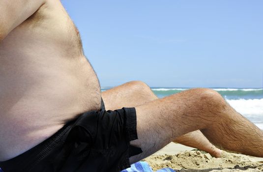 Unhealthy fat man sitting on the beach on a sunny day