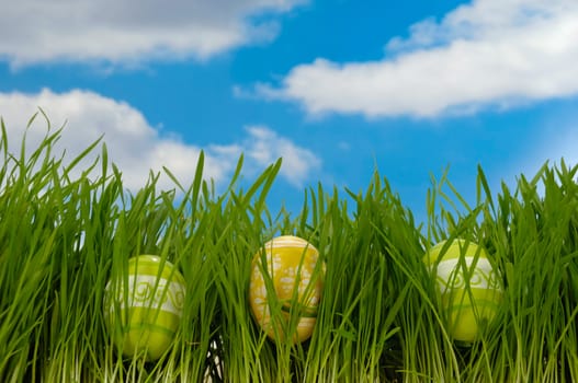 Painted easter eggs in green grass with a blue and cloudy sky.