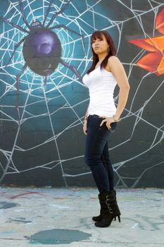 A beautiful young girl with lots of attitude stands in front of a graffiti spider on his web.