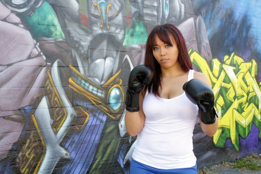 A lovely young female boxer stands ready in front of colorful graffiti.