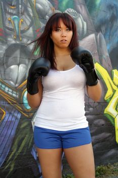 A lovely young female boxer stands ready in front of colorful graffiti.