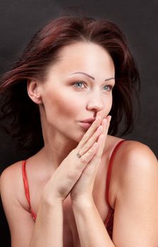 The model is in the center of the frame. She does not look at the camera. Hands folded in her mouth. Black background