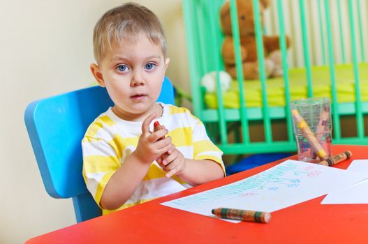 Little cute boy draws with many crayons in the nursery