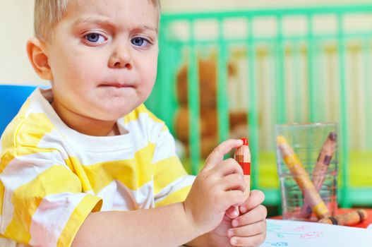 Little cute boy draws with many crayons in the nursery