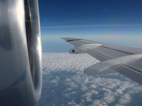 Flying plane wing and motor upon clouds in a deep blue sky