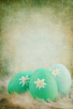 Textured Easter eggs in a nest of feathers against a green vintage background with room for copyspace. Extreme shallow DOF.
