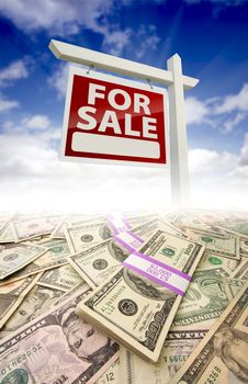 Stacks of Money Fading Off and For Sale Real Estate Sign Against Blue Sky with Clouds.