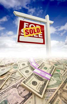 Stacks of Money Fading Off and Sold For Sale Real Estate Sign Against Blue Sky with Clouds.